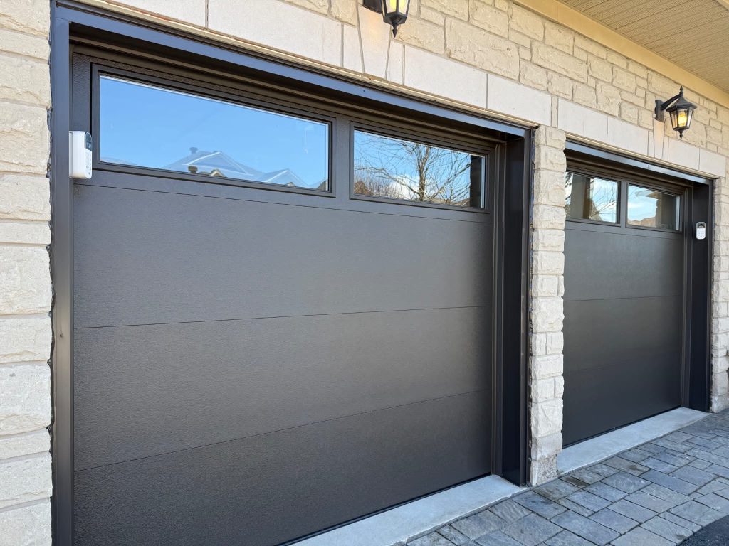 Charcoal double garage doors with upper windows on a stone facade
